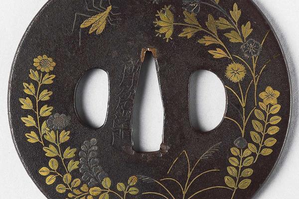 Detail of an 18th century metallic, round, Japanese tsuba, or sword guard, with autumn flowers and insects