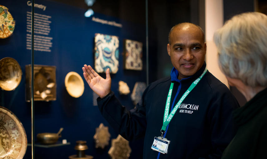 Museum staff member and volunteer stand in front of a case of museum objects on display